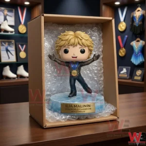 Ilia Malinin 2026 World Champion Pop Figure 5 A close up shot of a collectible figure of an ice skater with a gold medal inside an open shipping box! It is surrounded by bubble wrap on a wooden surface! The background shows a shelf with skating items and medals!