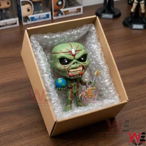 A green vinyl toy figure packed in a cardboard box with bubble wrap on a wooden table.