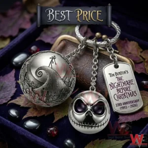 A silver anniversary keychain with three charms is shown! The charms feature a carved landscape sphere a skeleton head and a commemorative dog tag! It sits on purple velvet with leaves and stones!