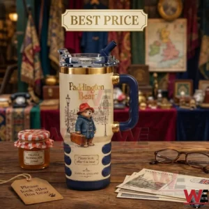 A large travel cup with a handle is displayed on a desk! It features Paddington Bear and is surrounded by a jar of marmalade postcards and glasses!