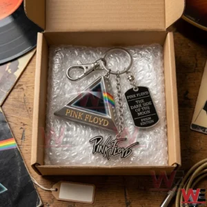 An open cardboard box containing a silver Pink Floyd keychain protected by bubble wrap is placed on a wooden desk near music equipment!