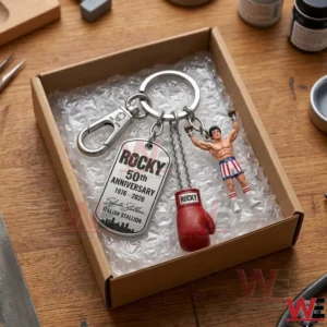 An overhead view of a metallic Rocky movie keychain with multiple charms packaged in a cardboard gift box with bubble wrap on a wooden surface!