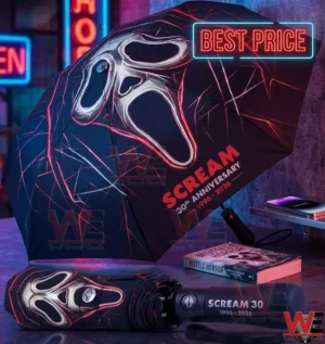 Close up of a Scream 30th anniversary umbrella with a glowing Ghostface mask design resting on a table next to a horror book and neon lights!