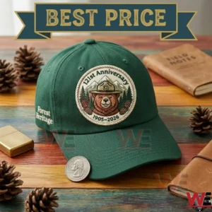 Close up shot of a forest green anniversary baseball cap with a bear ranger patch resting on a wooden table with pine cones and notebooks!