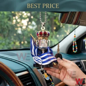 A silver trophy ornament with a red crown and a Real Sociedad flag hanging inside a car held by a hand next to an ignition key!
